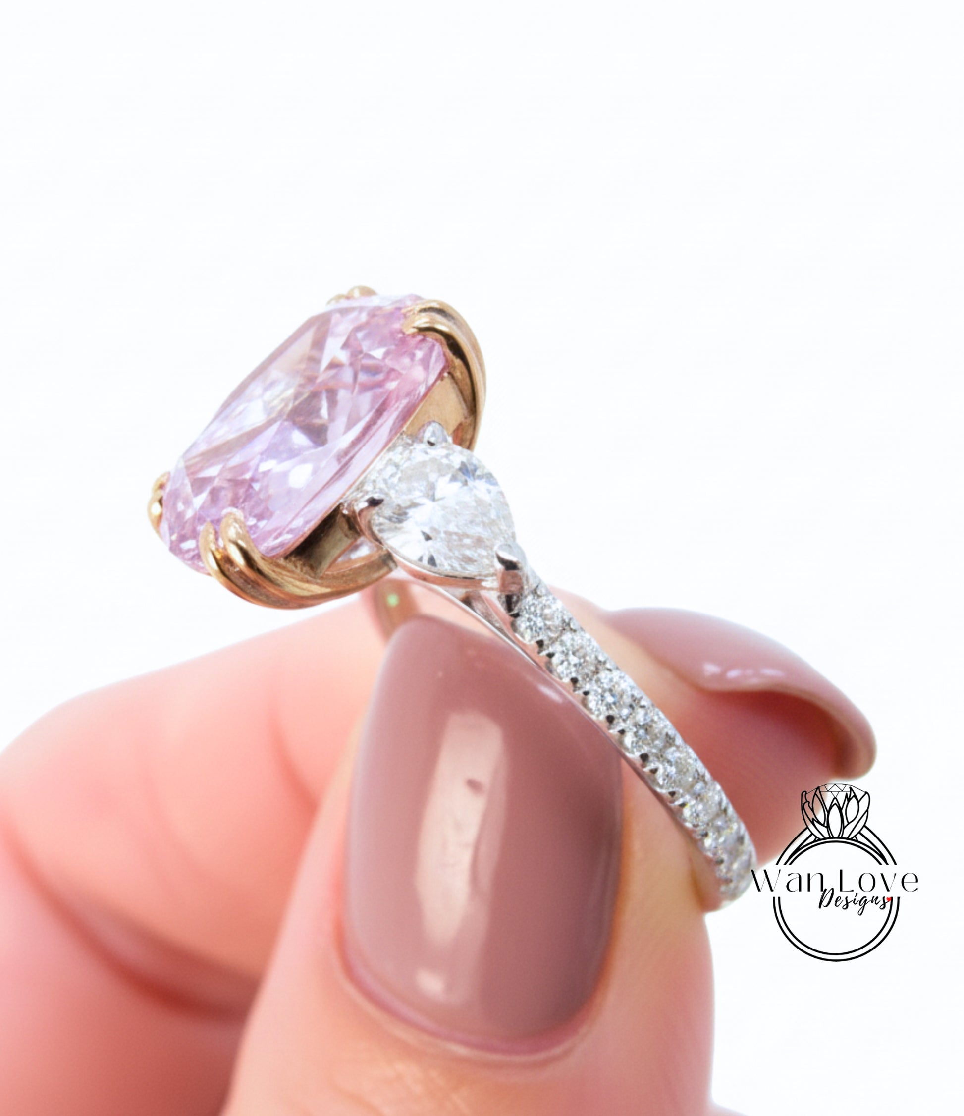A close-up of a person's hand holding a pink diamond engagement ring with a large central diamond and smaller diamonds around the band.