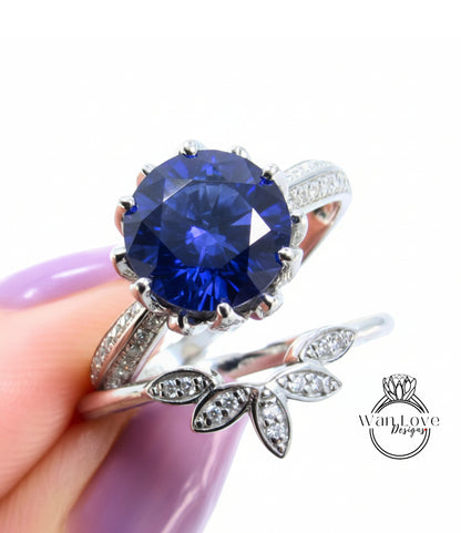 A close-up image of a person's hand holding a silver ring with a large blue gemstone, and a smaller ring with a leaf-shaped gemstone.