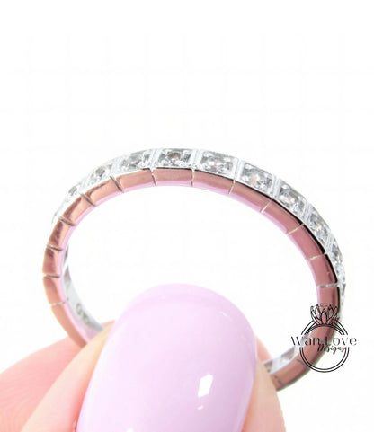 A close-up of a person's hand holding a pink nail polish bottle, with a ring featuring a row of diamonds on the finger.