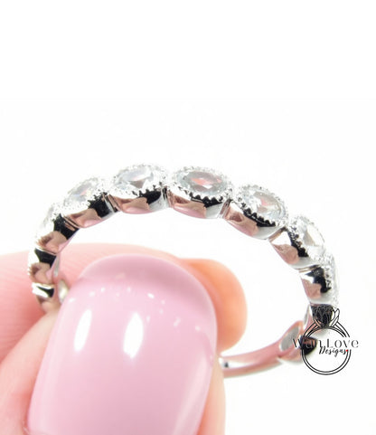 A close-up of a person's hand holding a silver ring with a row of round gemstones on it.