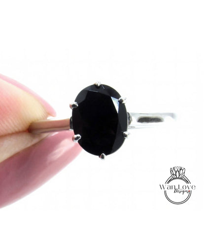 A close-up image of a person's hand holding a silver ring with a large oval-shaped black gemstone.