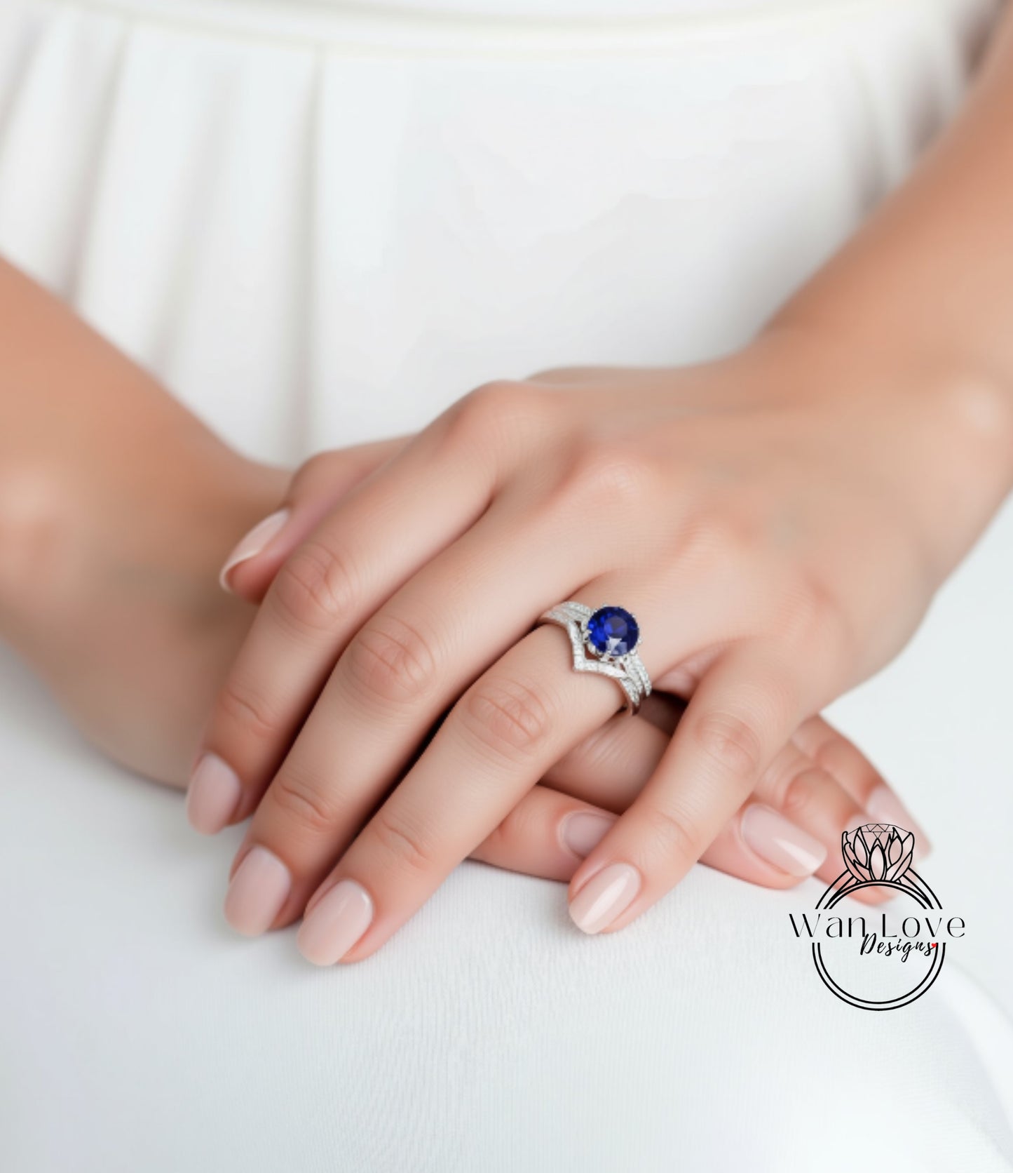 A close-up of a person's hand wearing a ring with a blue gemstone, resting on a white surface.