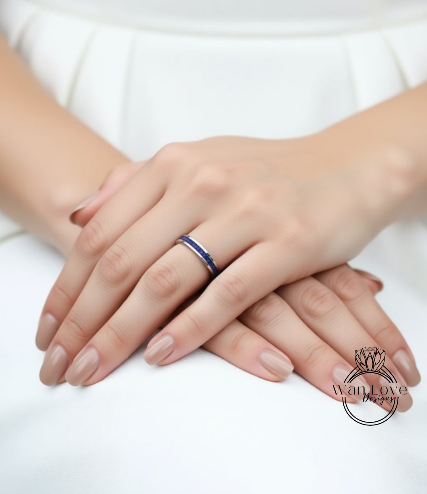 A close-up image of a person's hands wearing a ring, with the ring featuring a blue band and a small gemstone.