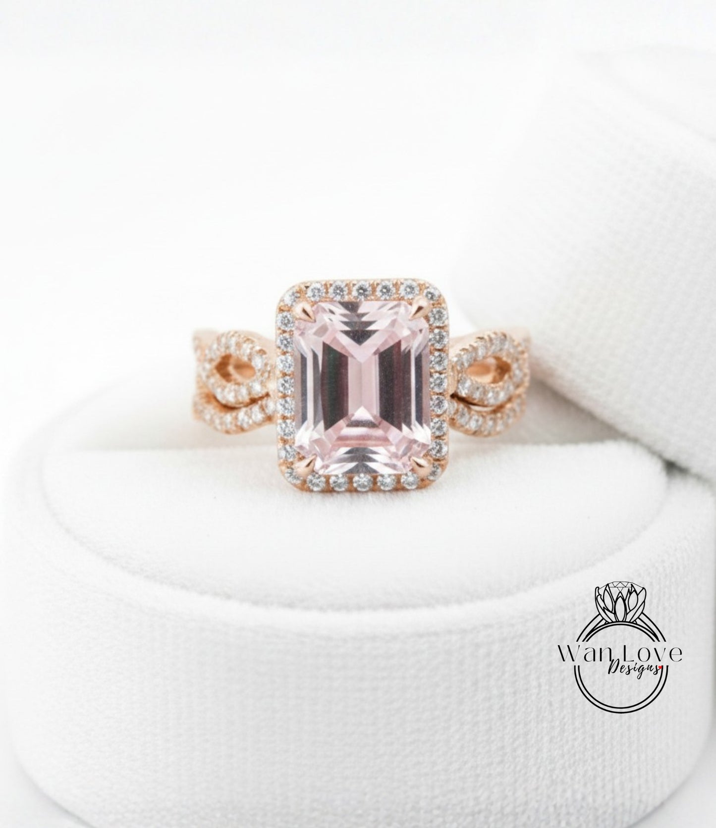 A pink gemstone engagement ring with a halo of diamonds set in a gold band, displayed on a white cloth.
