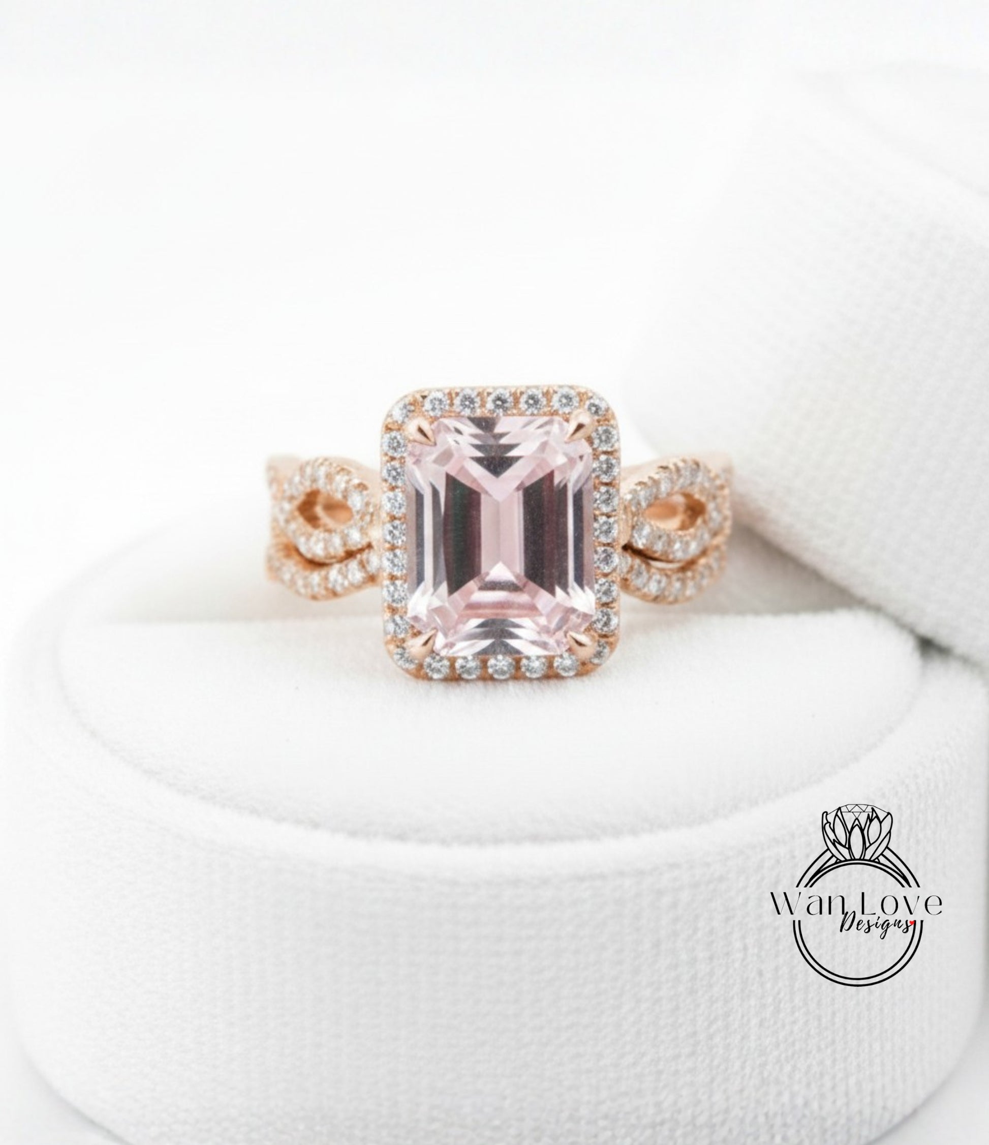 A pink gemstone engagement ring with a halo of diamonds set in a gold band, displayed on a white cloth.