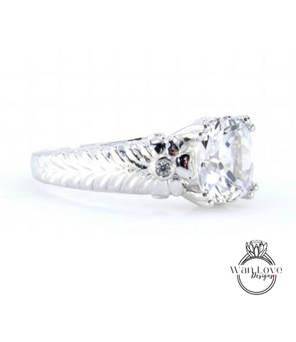 A close-up view of a silver ring with a large central diamond and a decorative leaf-like design on the band.