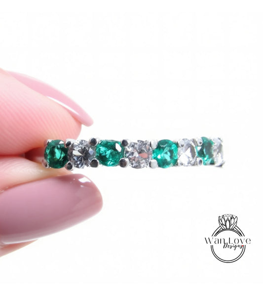 A hand holding a silver ring with a row of green and white gemstones.