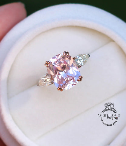 A close-up image of a pink diamond engagement ring with a large central diamond and two smaller diamonds on either side, displayed in a white jewelry box.