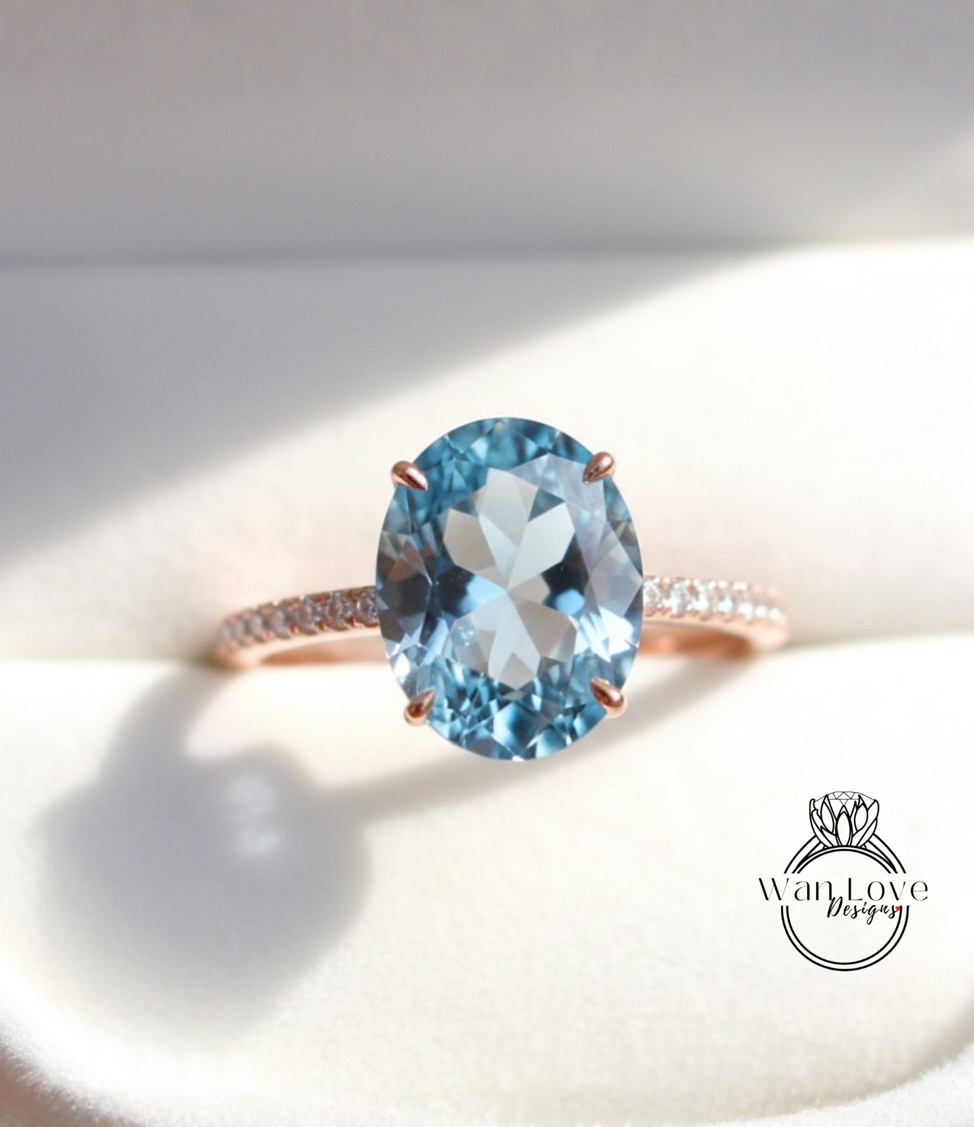 A close-up image of a rose gold ring with a large blue gemstone, likely an aquamarine, set in the center of the band.