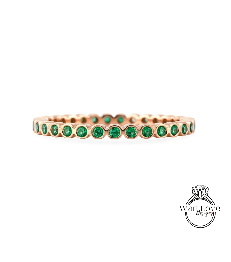 A gold-colored ring with a row of green gemstones, likely emeralds, set in the center.