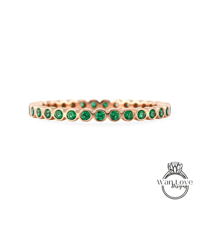 A gold-colored ring with a row of green gemstones, likely emeralds, set in the center.
