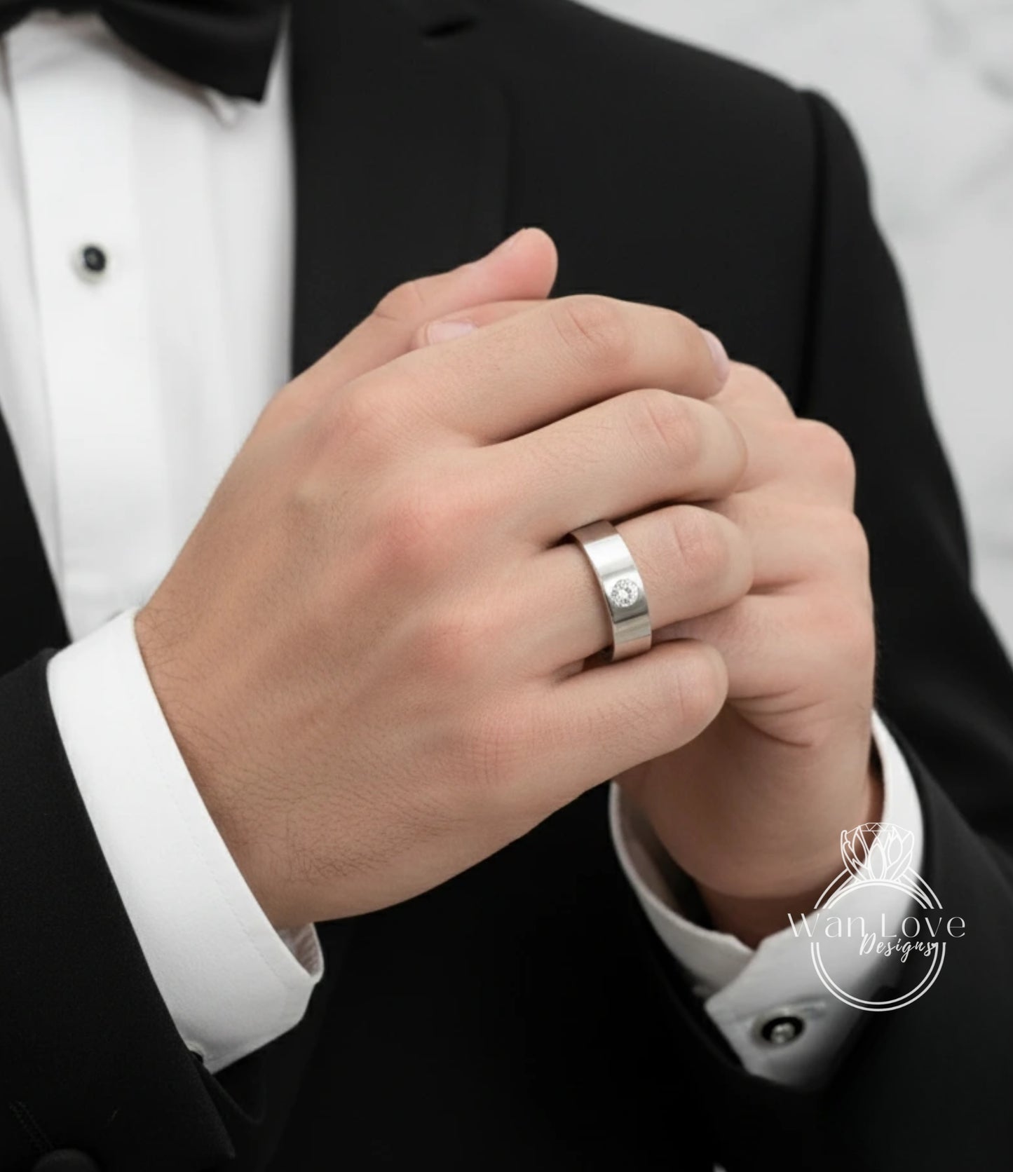 A close-up of a person's hand wearing a silver wedding ring, with a black suit jacket visible in the background.
