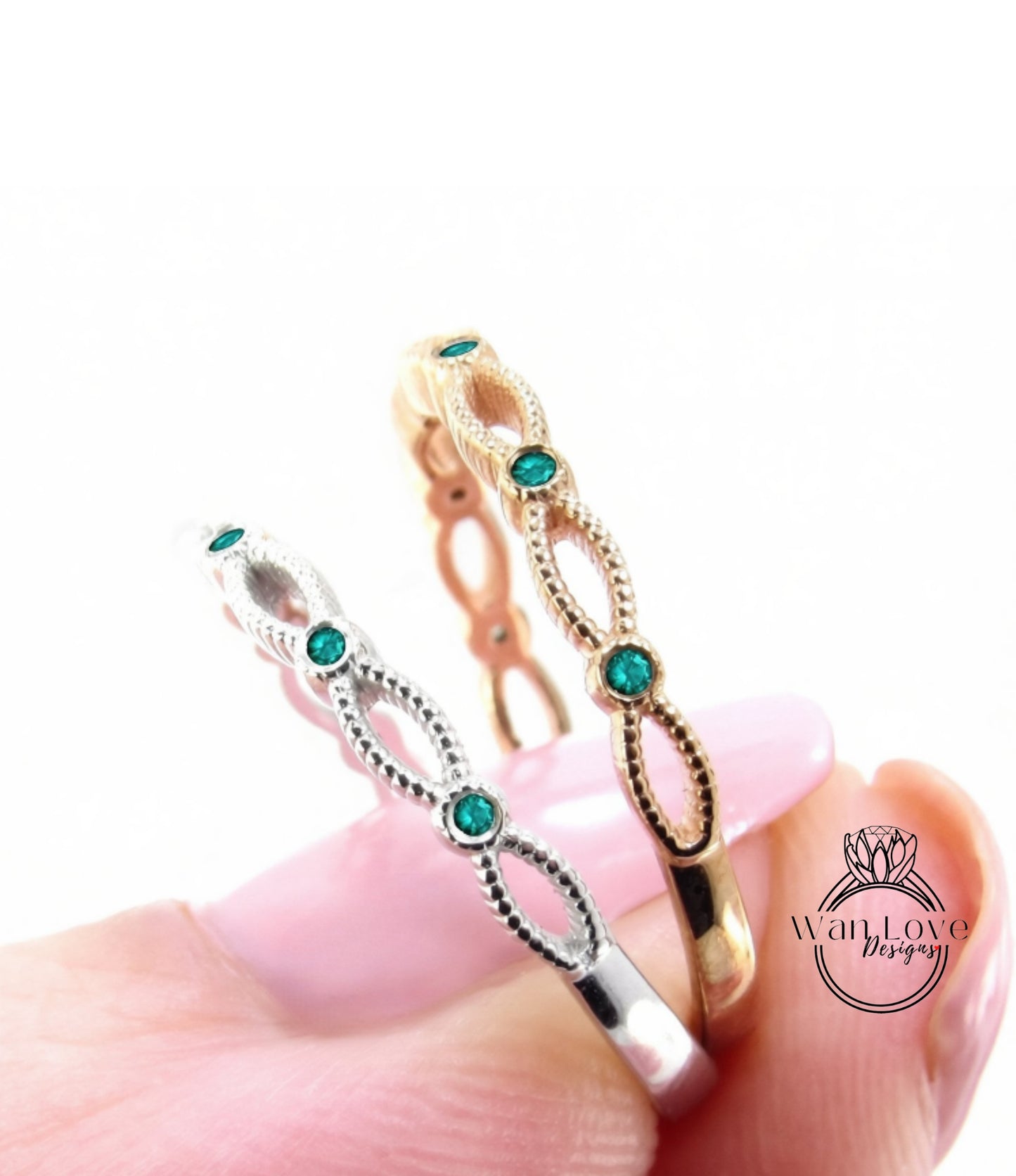 A close-up image of a person's hand holding two rings with green gemstones.