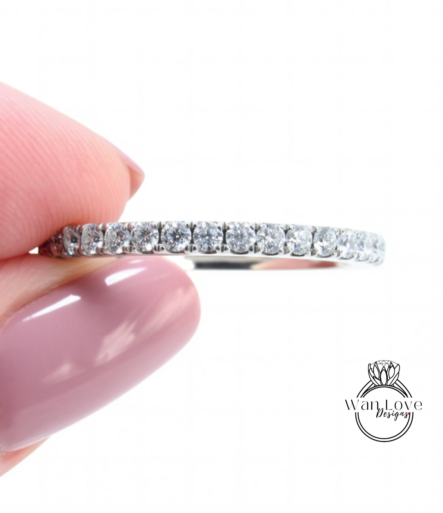 A close-up image of a person's hand holding a diamond band ring.