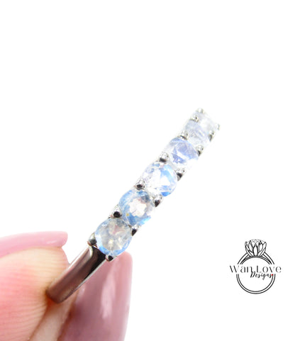 A close-up image of a person's hand holding a silver ring with a row of blue moonstone stones.