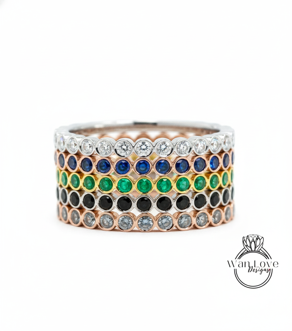 A stack of rings with various colored gemstones, including diamonds and emeralds, set in a silver band.