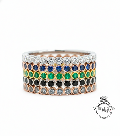 A stack of rings with various colored gemstones, including diamonds and emeralds, set in a silver band.