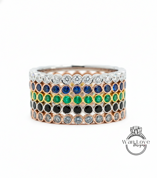A stack of rings with various colored gemstones, including diamonds and emeralds, set in a silver band.