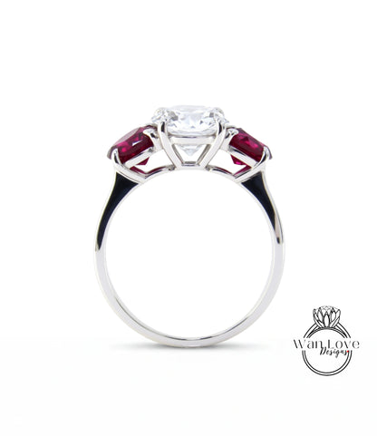 A silver engagement ring with a large central diamond surrounded by two smaller diamonds on either side, set in a silver band with a red gemstone.
