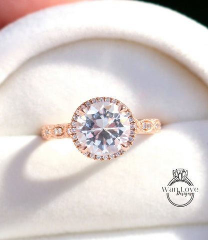A close-up image of a beautiful engagement ring with a large, clear gemstone set in a halo of smaller diamonds, displayed in a white box.