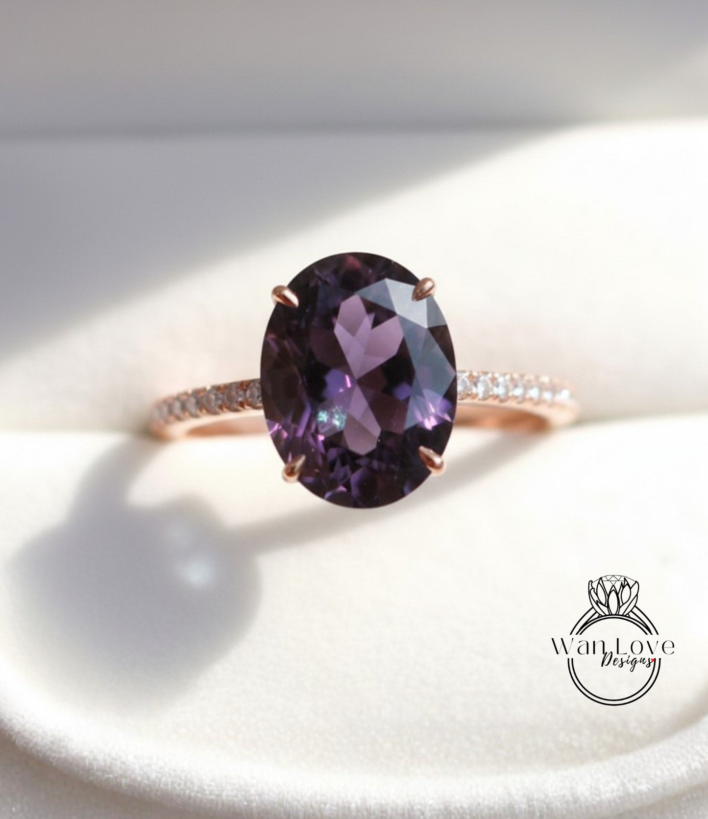 A close-up image of a rose gold ring with a large oval-shaped purple gemstone, such as an amethyst, set in the center of the band.