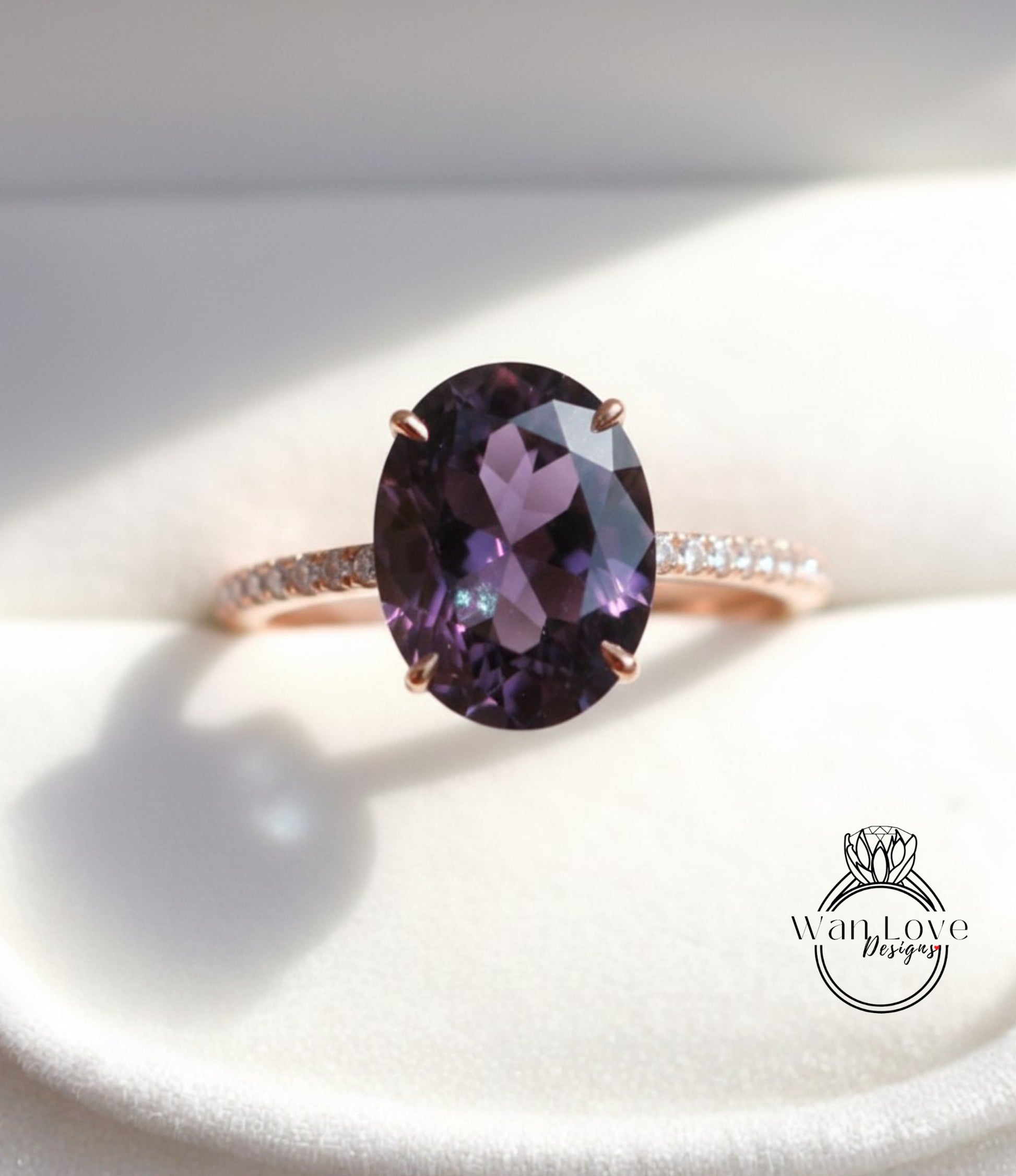 A close-up image of a rose gold ring with a large oval-shaped purple gemstone, such as an amethyst, set in the center of the band.