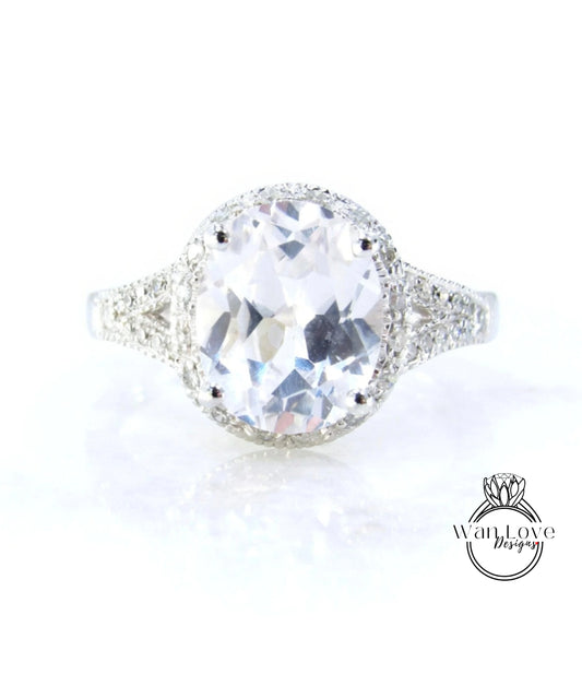A large, clear gemstone ring with a halo of smaller diamonds around the center stone.
