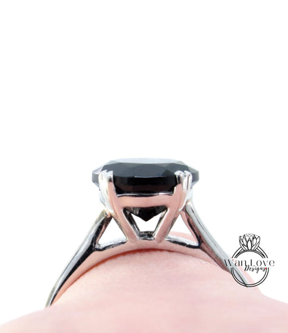 A close-up view of a silver ring with a large black gemstone, likely a diamond, set in the center of the band.