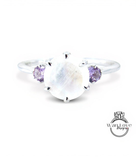 A silver ring with a large moonstone and two purple gemstones on either side.