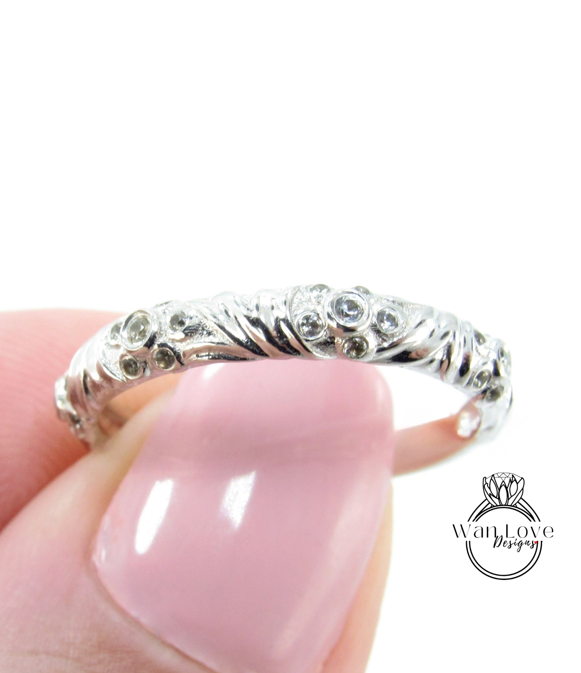 A close-up image of a person's hand holding a silver ring with a decorative design featuring small diamonds or gemstones.