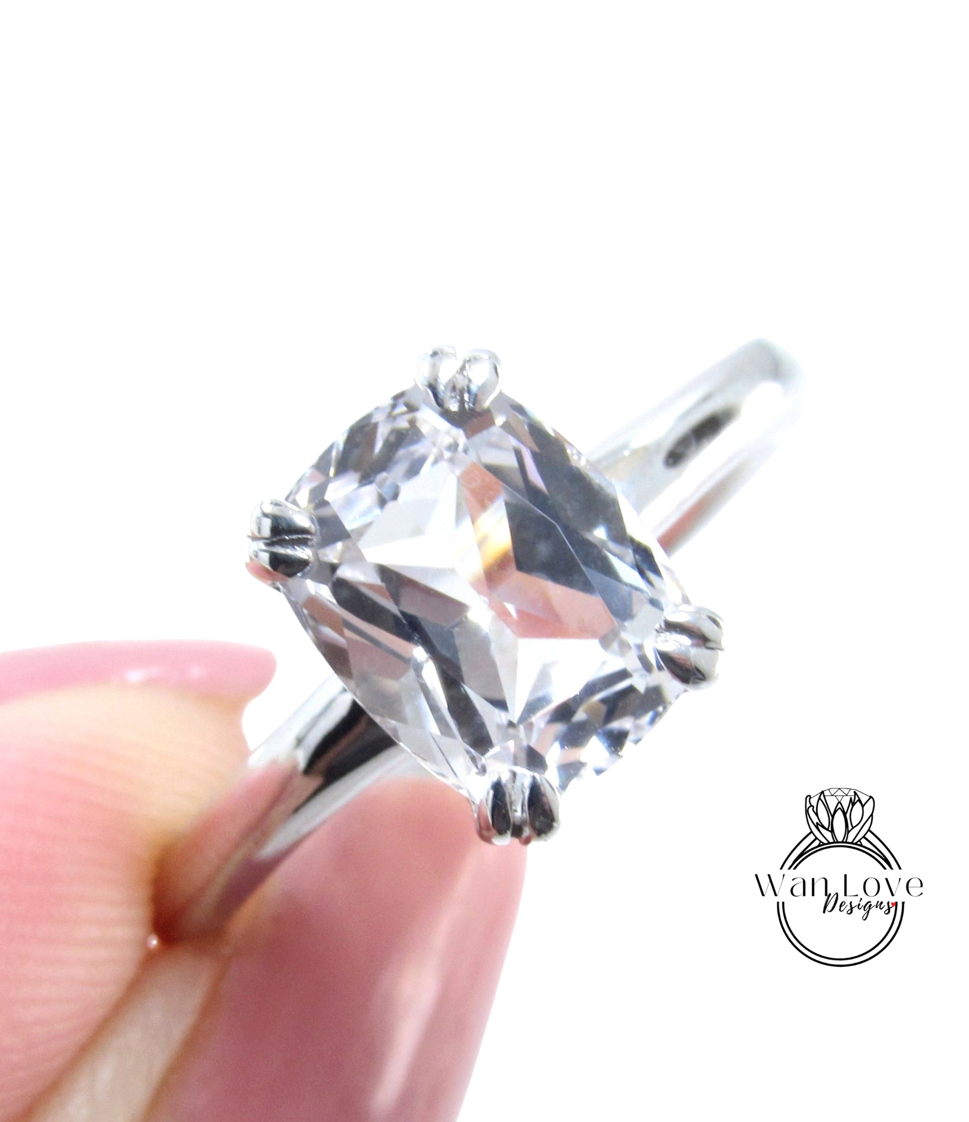 A close-up of a person's hand holding a diamond engagement ring with a large, clear gemstone.