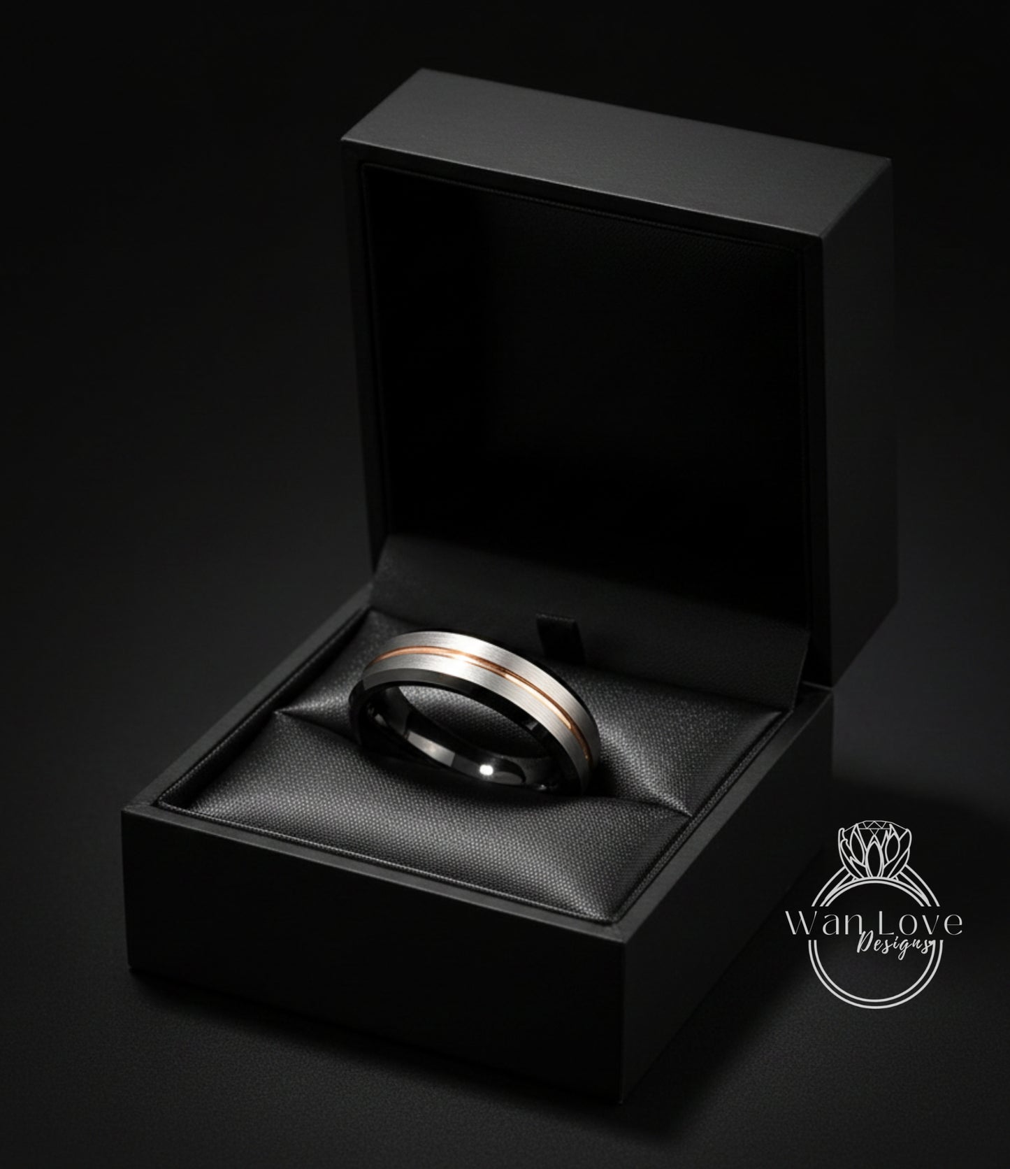 A black jewelry box containing a silver and gold ring, placed on a black surface against a dark background.
