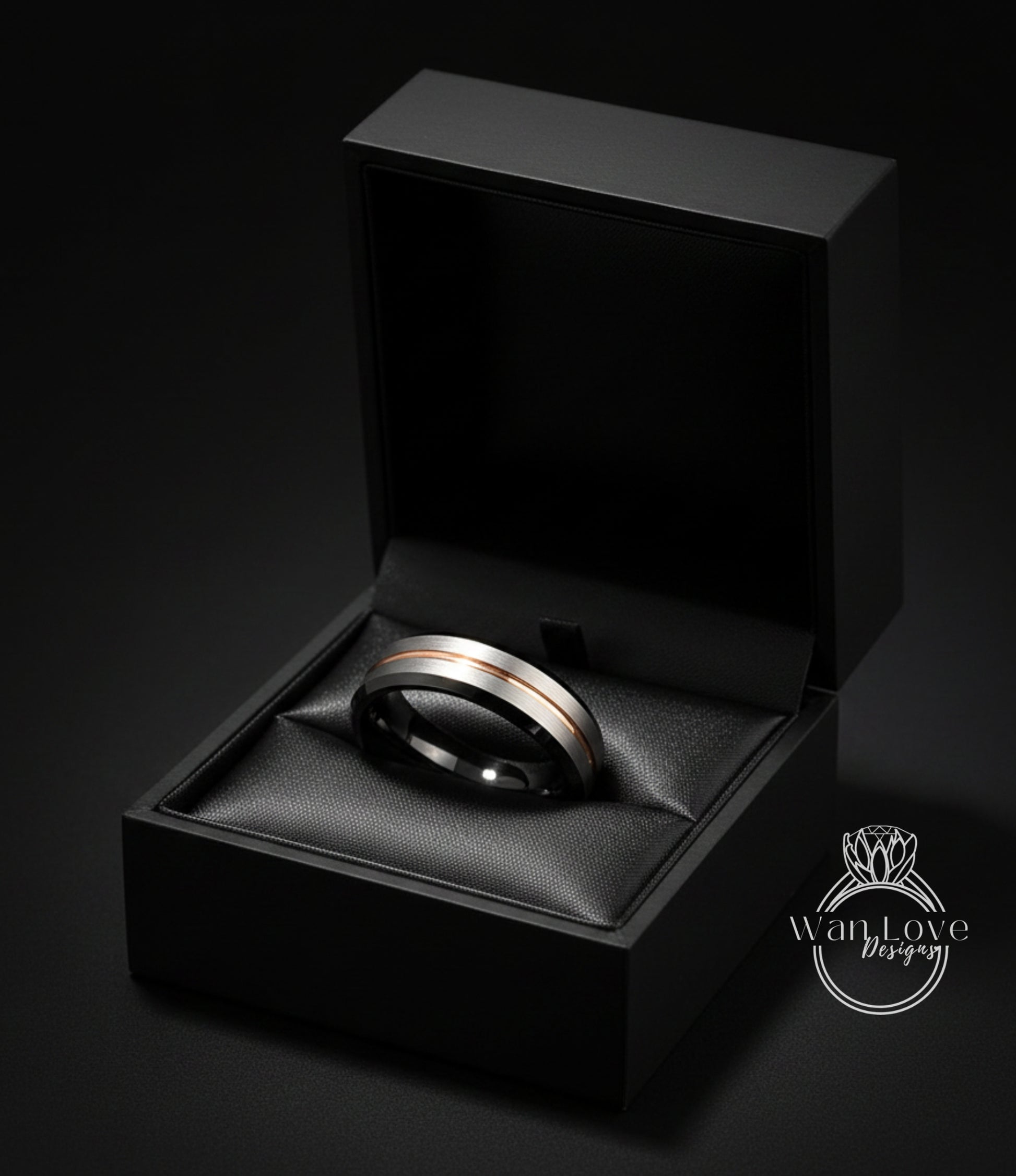 A black jewelry box containing a silver and gold ring, placed on a black surface against a dark background.