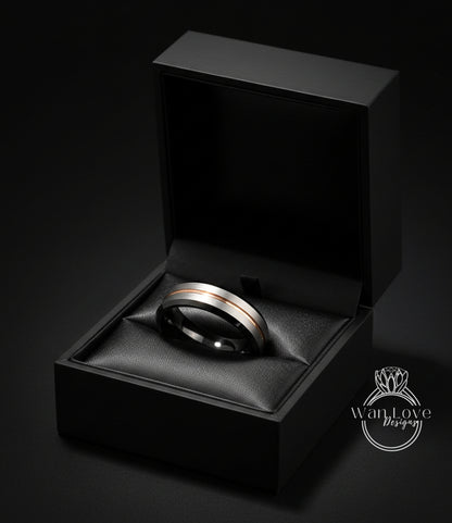 A black jewelry box containing a silver and gold ring, placed on a black surface against a dark background.