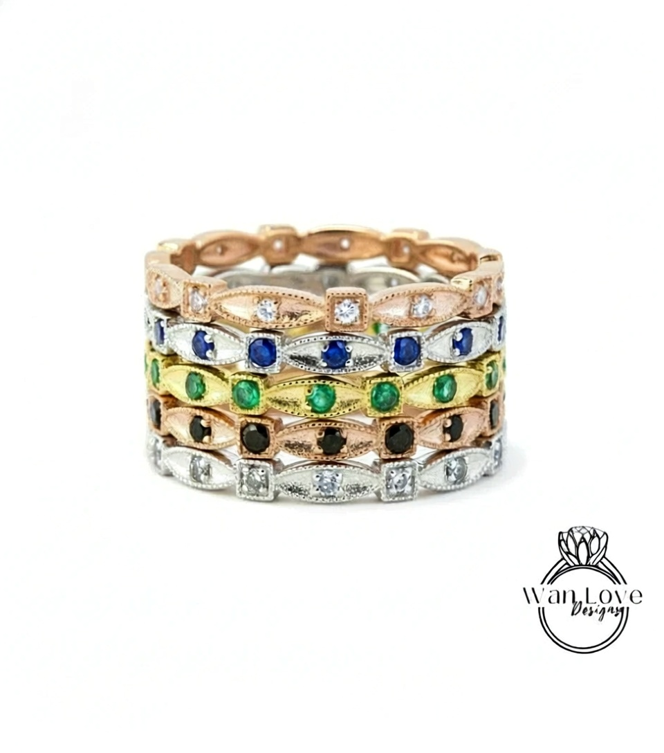 A stack of rings with various colored gemstones, including diamonds and emeralds, set in a gold or silver band.