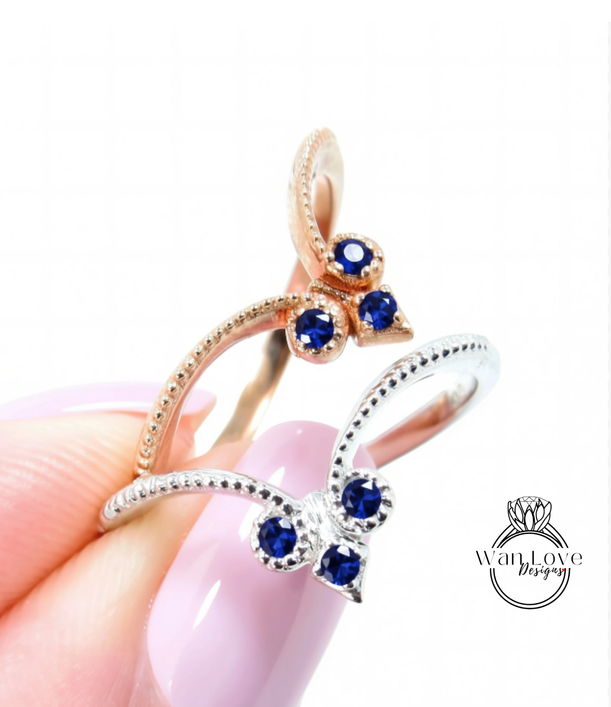A close-up image of a person's hand holding a ring with a butterfly design, featuring blue gemstones.