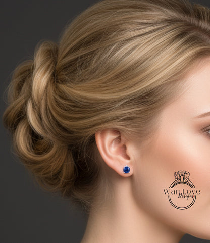 A close-up of a woman's face with her hair styled in a bun and a pair of blue earrings visible.
