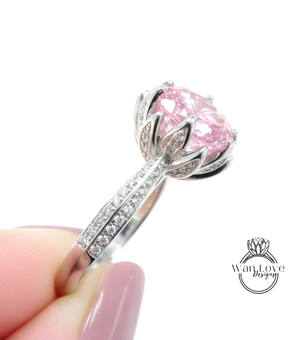 A close-up of a person's hand holding a silver ring with a large pink gemstone, likely a diamond.