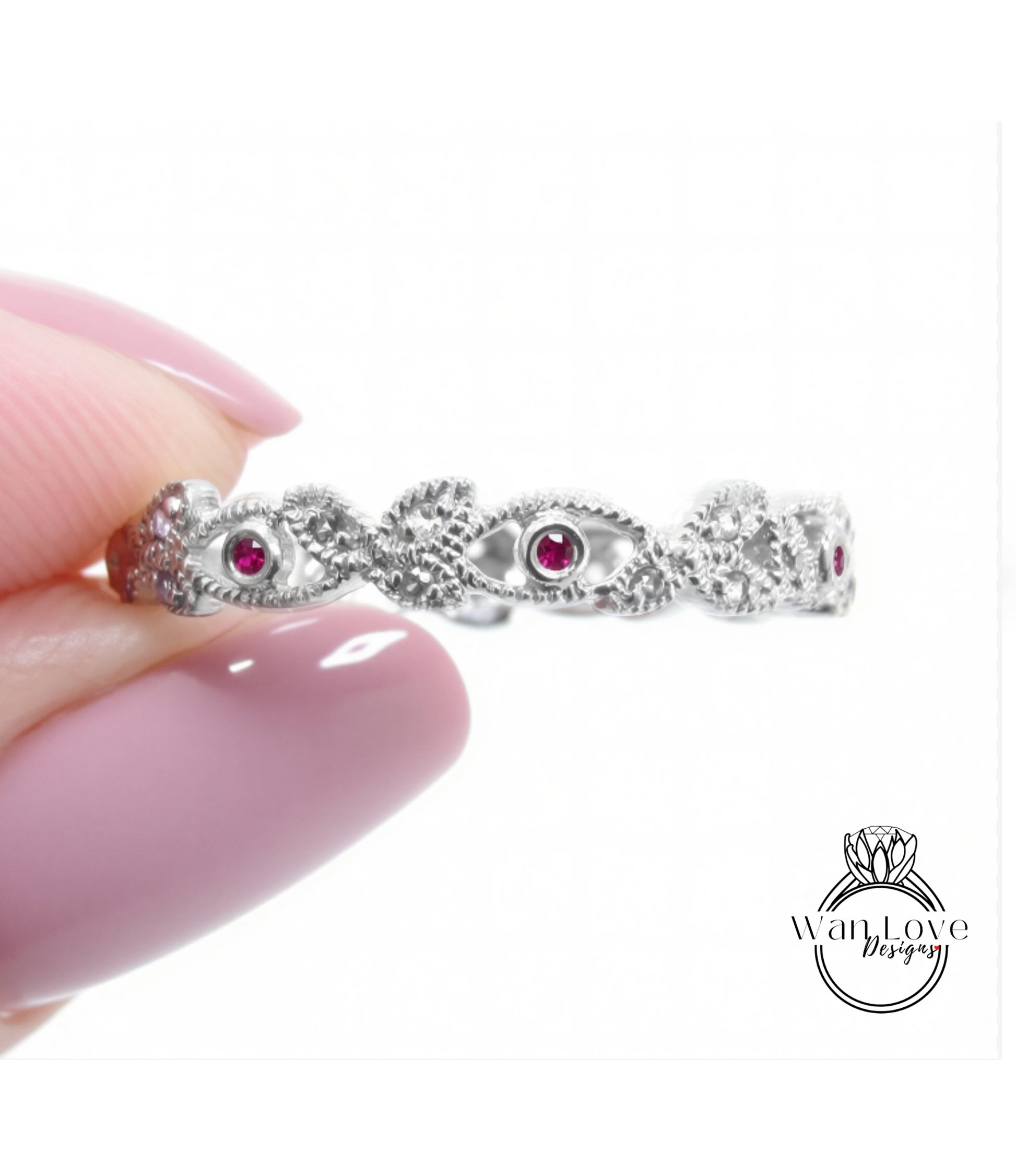 A hand holding a silver ring with a floral design and red gemstones.