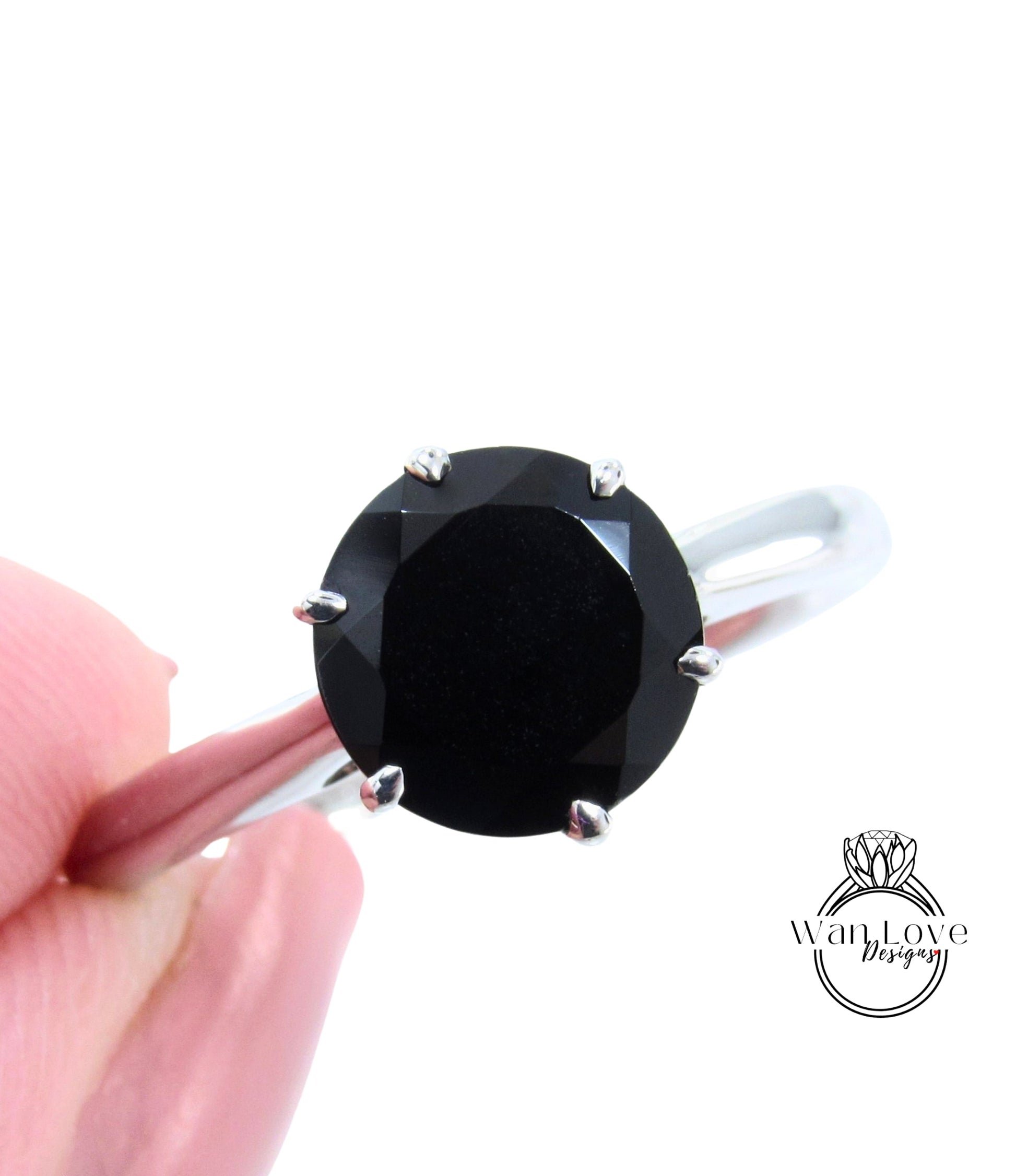 A close-up image of a person's hand holding a ring with a large black diamond as the centerpiece.