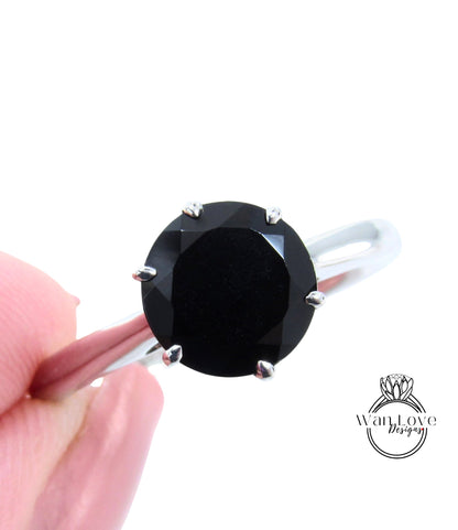 A close-up image of a person's hand holding a ring with a large black diamond as the centerpiece.