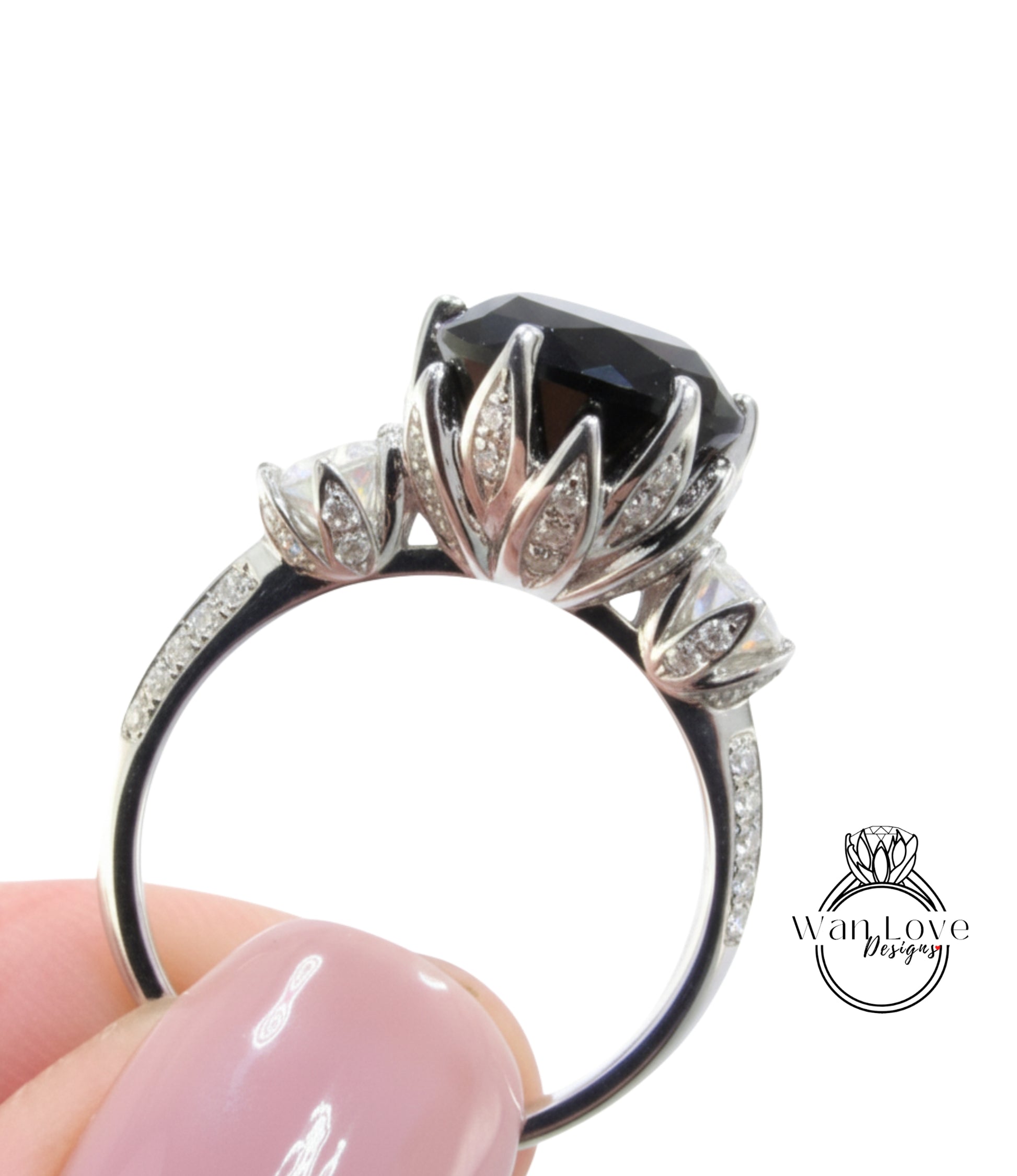 A close-up of a person's hand holding a silver ring with a large black gemstone and intricate floral designs.