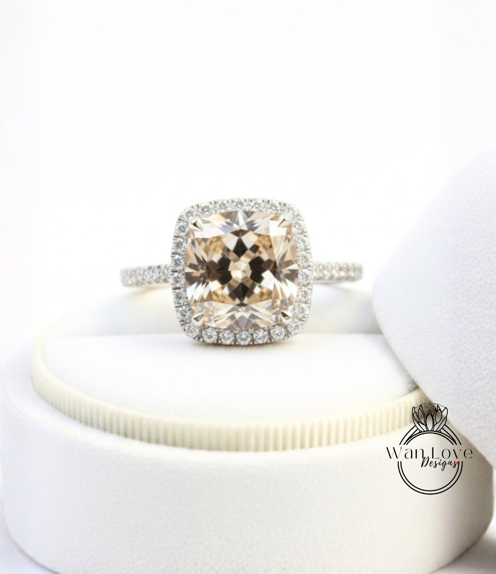 A large, round, beige-colored diamond ring with a halo of smaller diamonds around the center stone, displayed on a white pedestal.