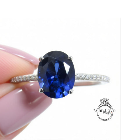 A close-up image of a person's hand holding a ring with a large blue gemstone, likely a sapphire or blue topaz.