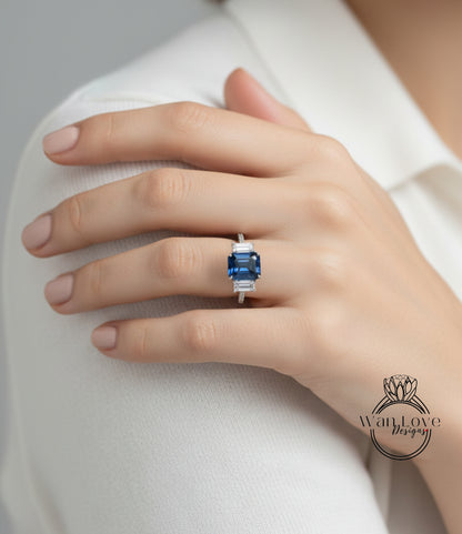A close-up of a person's hand wearing a ring with a large blue gemstone, resting on a white shirt.