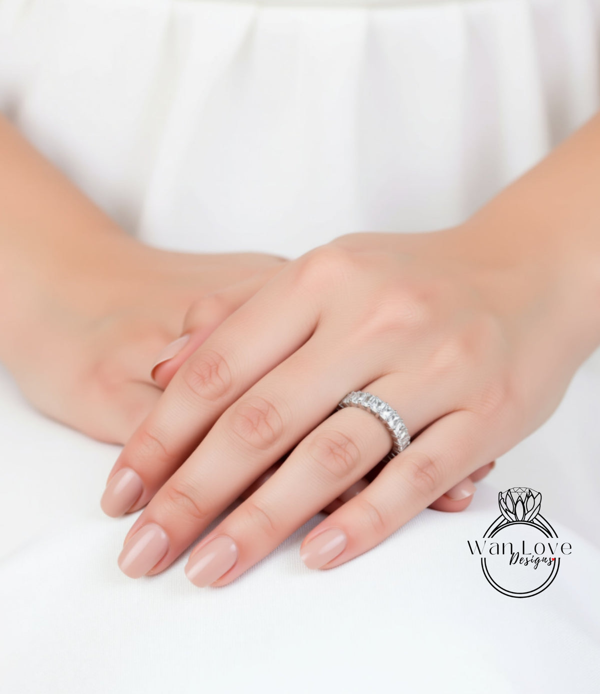 A close-up of a person's hands wearing a diamond ring, with a white background.