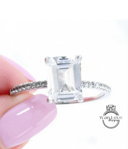 A close-up of a person's hand holding a diamond engagement ring with a large, clear gemstone.