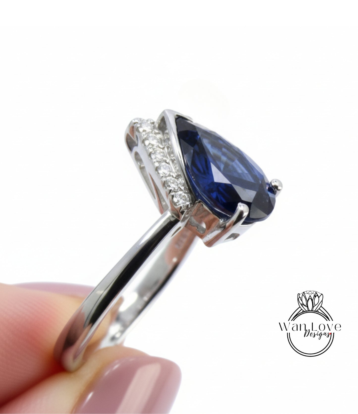 A close-up image of a person's hand holding a silver ring with a large blue gemstone, likely a sapphire, set in a diamond-encrusted band.