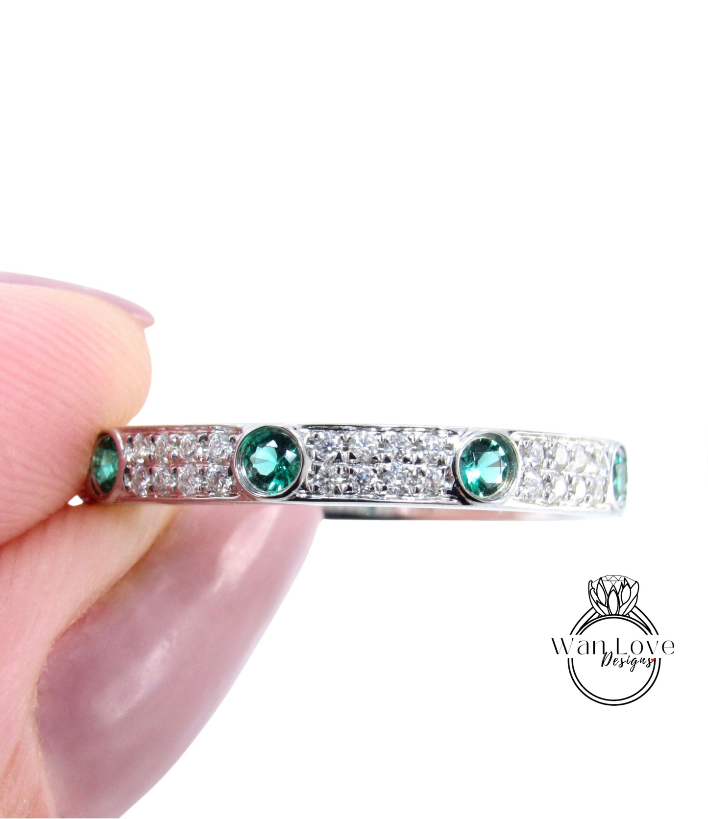 A hand holding a silver ring with green gemstones.