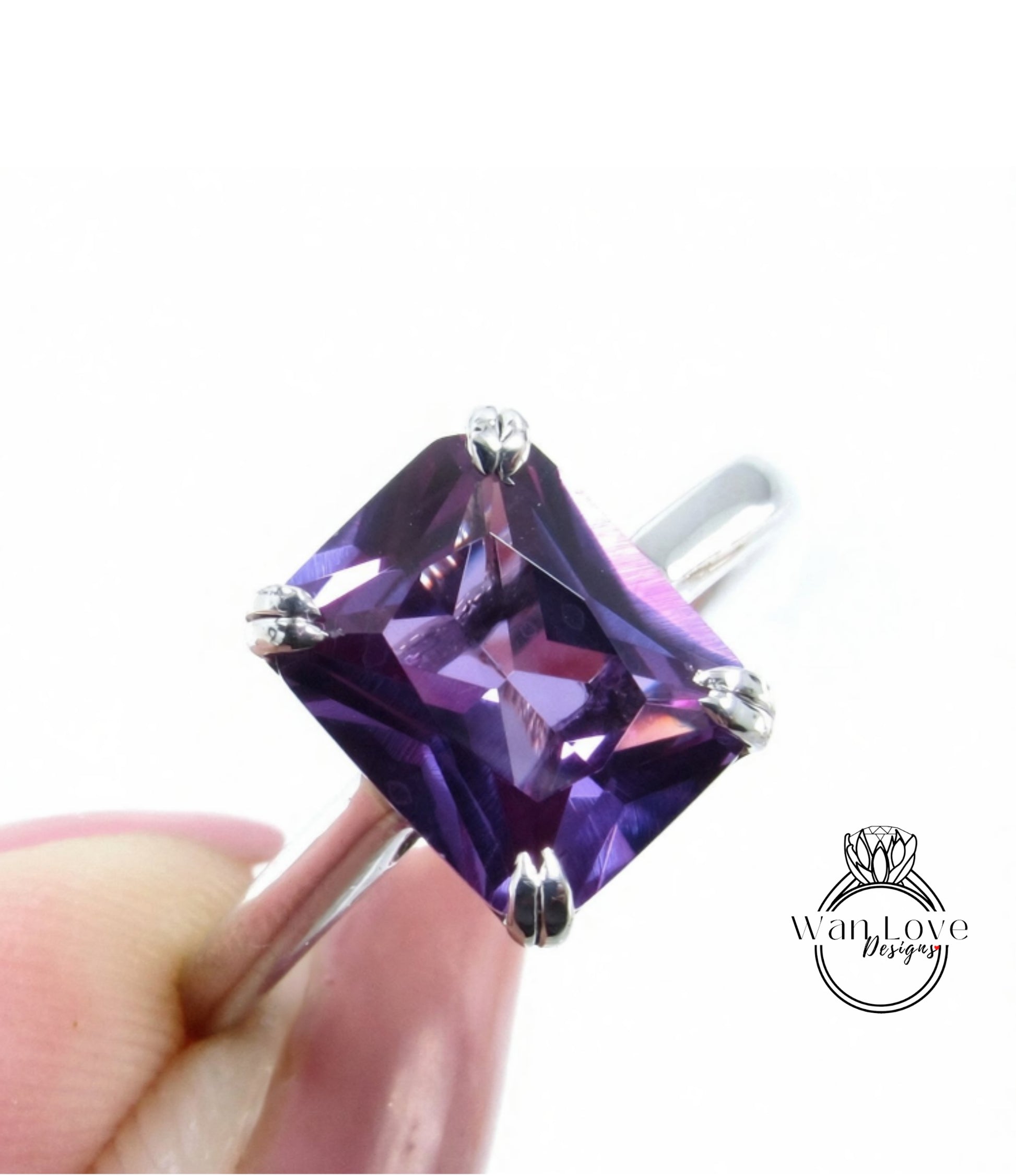 A close-up image of a person's hand holding a ring with a large, square-cut purple gemstone.